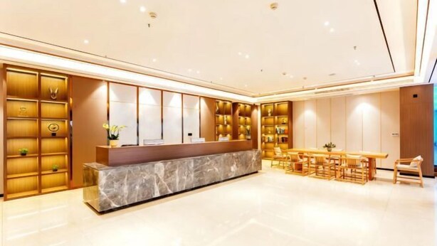 Un moderno vestíbulo de hotel con una recepción de mármol, estanterías de madera con objetos decorativos y un área de comedor con mobiliario de madera.
