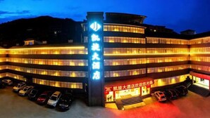 Un hotel de varios pisos con un letrero iluminado llamativo, una zona de estacionamiento techada y una entrada visible.