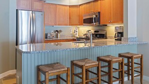 A modern kitchen with wooden cabinets, stainless steel appliances, a granite countertop, and bar stools. - Ski-In/Out at Okemo | 3BR Ledgewood w/ Fireplace (Ludlow)