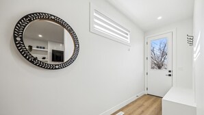 A hallway with a round mirror, a white door, and a light switch on the wall. - Ultimate Group Stay, 3 King Beds, 2 Suites (Calgary)