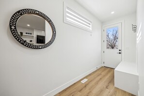 Um corredor com um espelho redondo, uma porta branca e um interruptor de luz na parede.