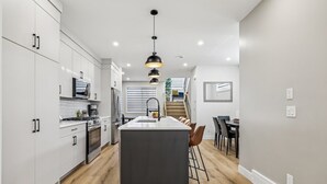 A modern kitchen with white cabinets, a central island, and a dining area with chairs. - Ultimate Group Stay, 3 King Beds, 2 Suites (Calgary)