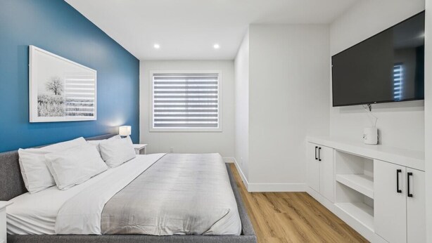 A modern bedroom with a bed, a TV, and a window with blinds. - Ultimate Group Stay, 3 King Beds, 2 Suites (Calgary)