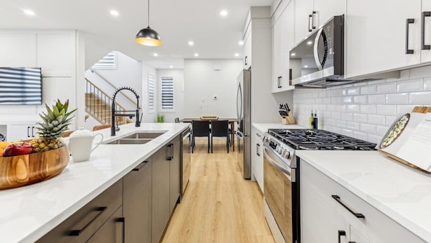 A modern kitchen with white cabinetry, a wooden floor, a stainless steel stove, and a microwave.
