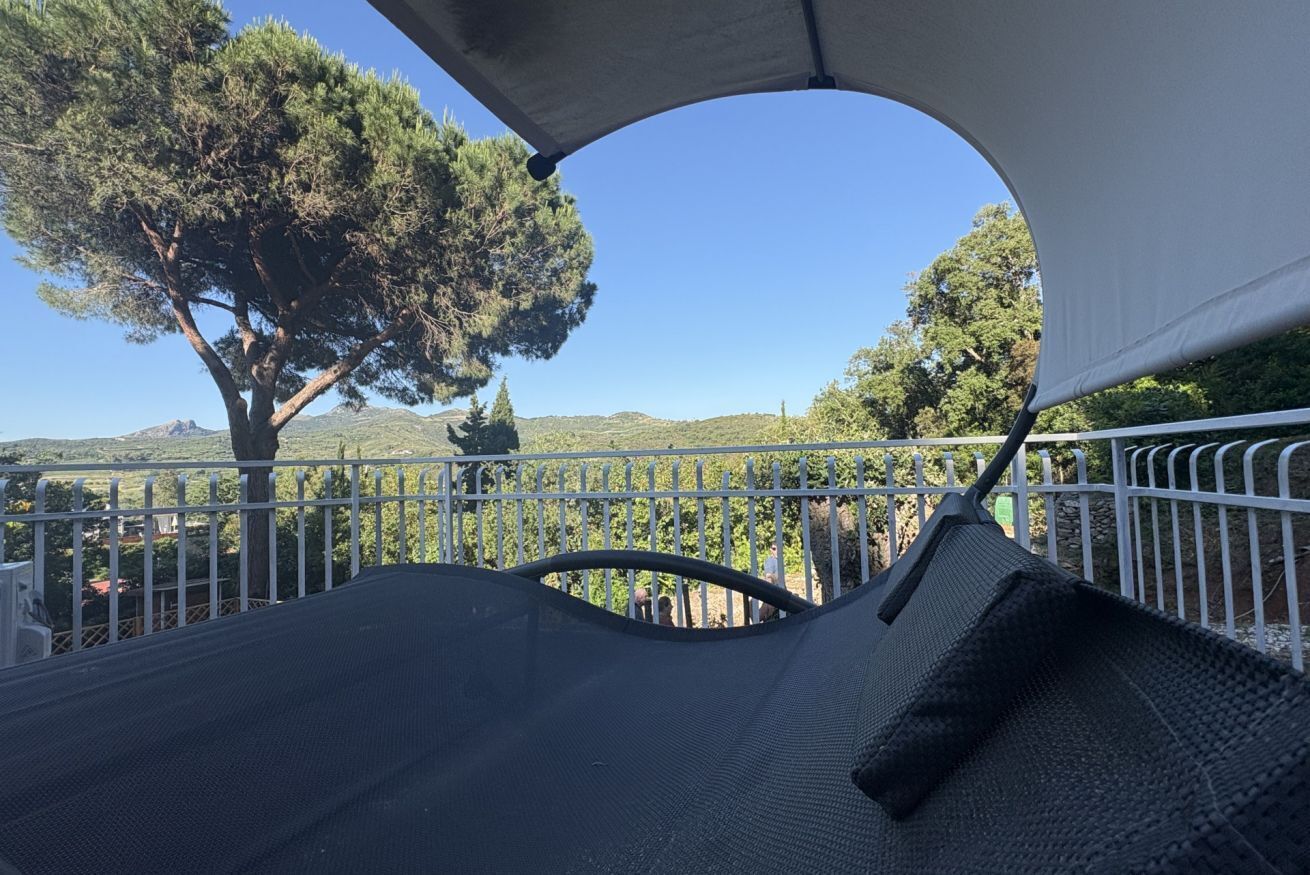 A covered outdoor seating area with a view of a tree and hills.