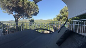 Un espace extérieur abrité, aménagé avec des sièges, et offrant une vue sur un arbre et des collines.