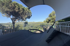 Un'area salotto esterna coperta con vista su un albero e delle colline.