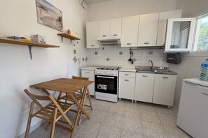 A kitchen with white cabinets, a stove, a sink, and a small refrigerator. There is a wooden table with chairs.