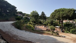 Un quartier résidentiel avec une allée en gravier, une terrasse clôturée et une maison avec un toit rouge.