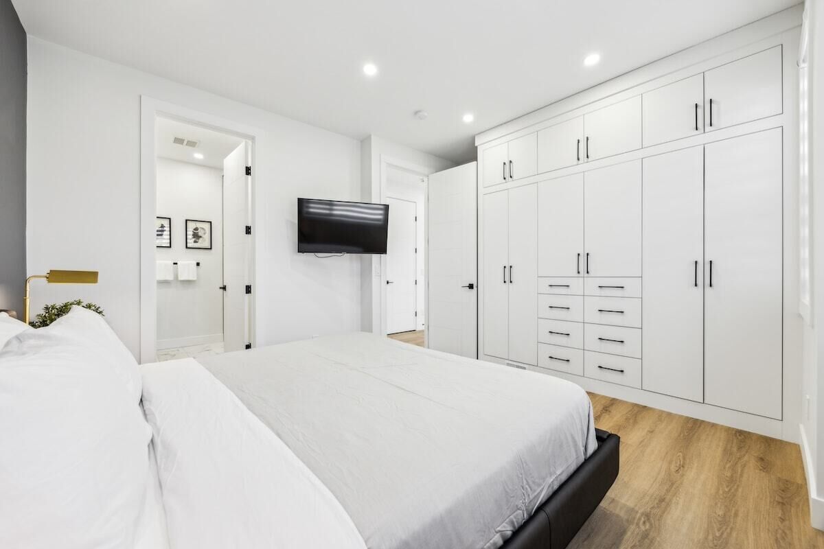 Ein modernes Schlafzimmer mit einem großen Bett, einem weißen Kleiderschrank und einem an der Wand befestigten Flachbildfernseher.