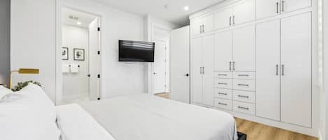 A modern bedroom with a large bed, white wardrobe, and a flat-screen TV mounted on the wall.