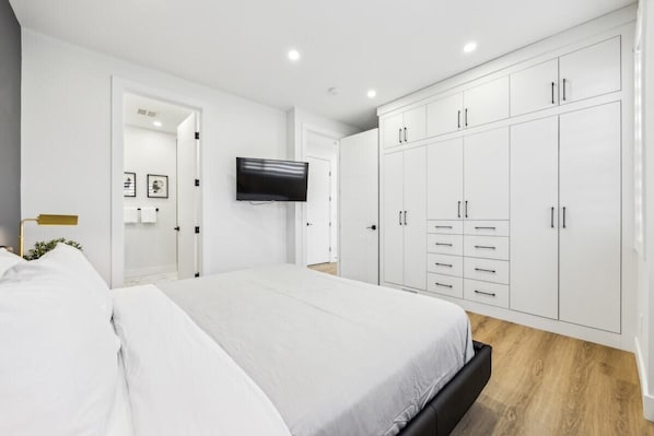 Un dormitorio moderno con una cama grande, un armario blanco y un televisor de pantalla plana montado en la pared.