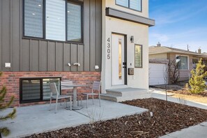 A modern two-story house with a visible garage door, a front porch with a bench, and a well-maintained front yard with mulch and a small tree. - Rare Find-Dual Suites, 3 Kings & Prime Location (Calgary)