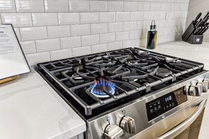 Una cocina con estufa de acero inoxidable, un reloj digital y un salpicadero blanco de azulejos.