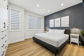 A modern bedroom with a large bed, bedside tables, and a wall-mounted artwork. - Rare Find-Dual Suites, 3 Kings & Prime Location (Calgary)