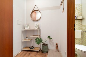 Un baño con inodoro, lavamanos, espejo y repisa con planta en maceta y un libro.