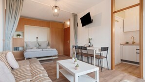 Ein modernes Wohnzimmer mit einer Couch, einem Esstisch mit Stühlen, einer Küchenzeile und einem an der Wand montierten Fernseher.