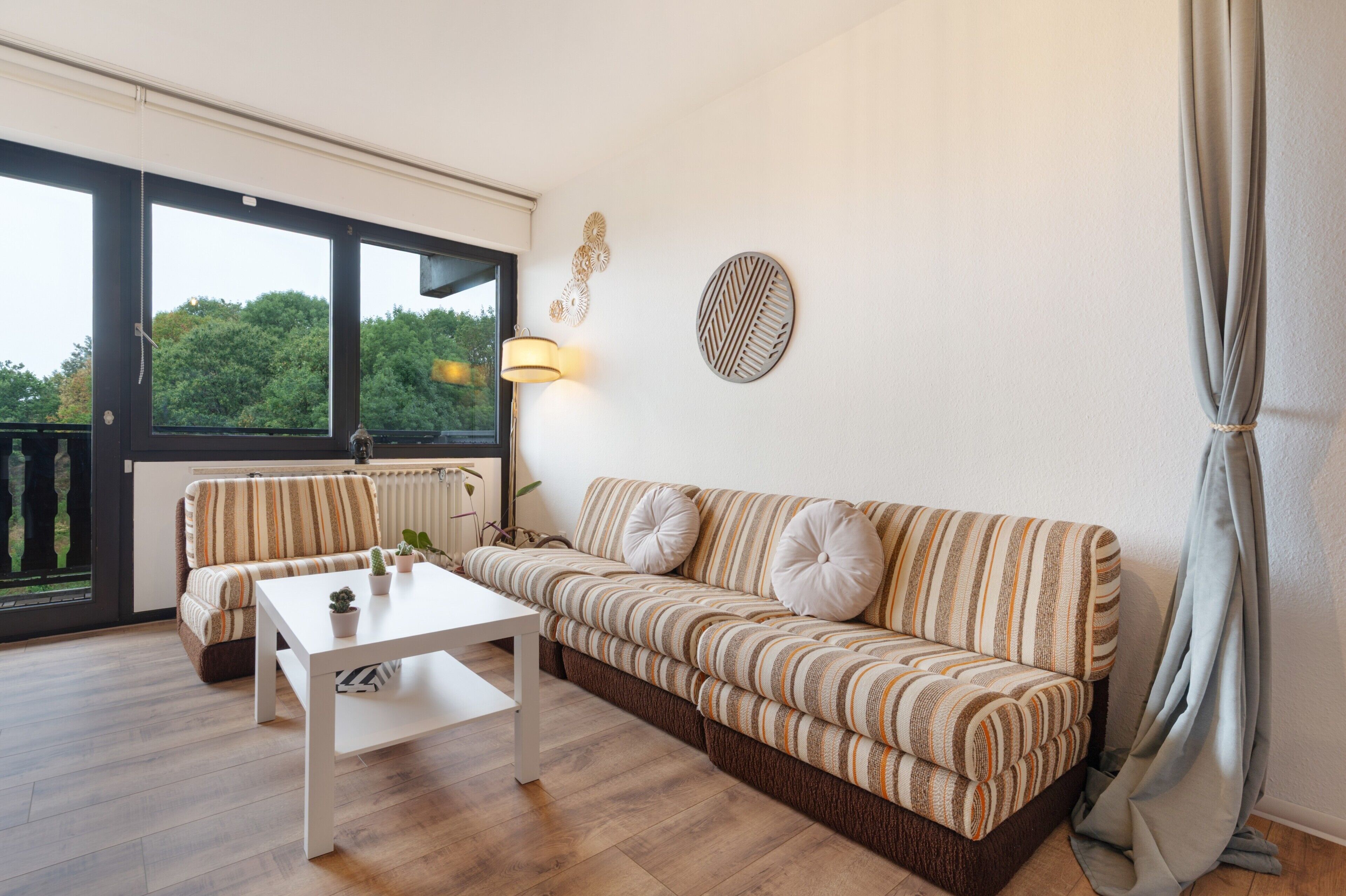 Ein modernes Wohnzimmer mit einem gestreiften Sofa, einem weißen Couchtisch und Blick durch große Fenster.