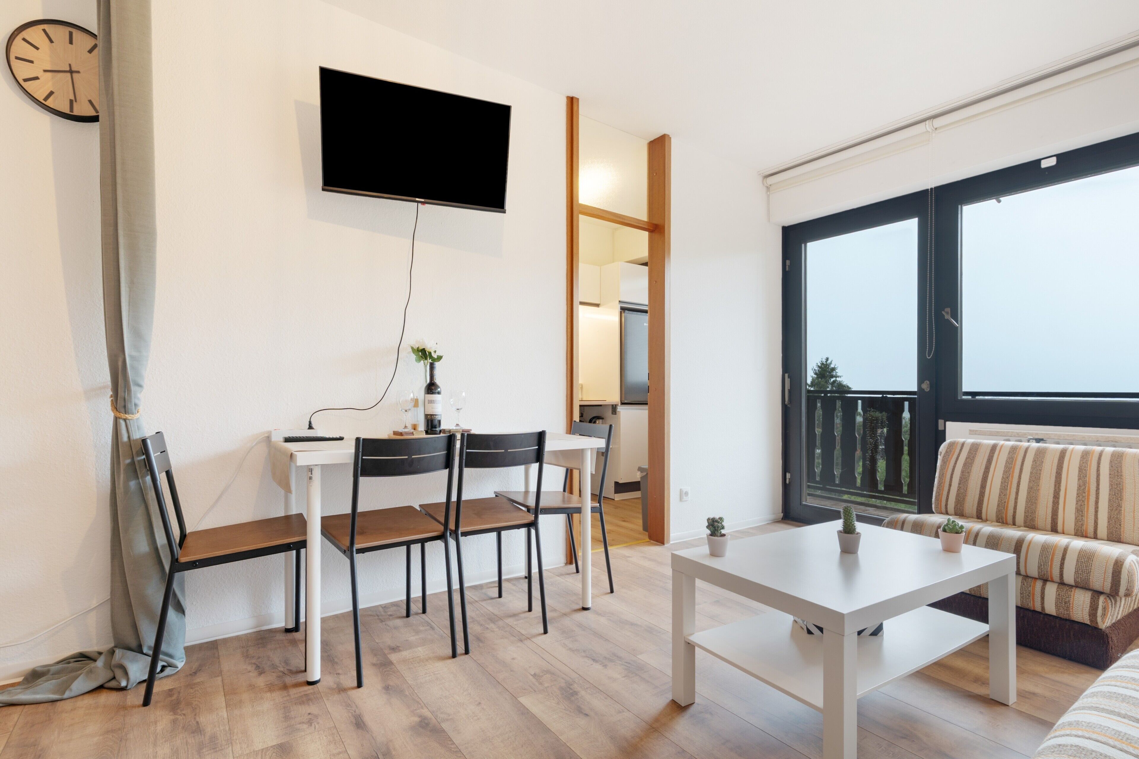 Ein modernes Wohnzimmer mit Essbereich, einem an der Wand befestigten Flachbildfernseher, einer Couch und einem großen Fenster mit Blick.