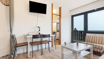 Ein modernes Wohnzimmer mit Essbereich, einem an der Wand befestigten Flachbildfernseher, einer Couch und einem großen Fenster mit Blick.