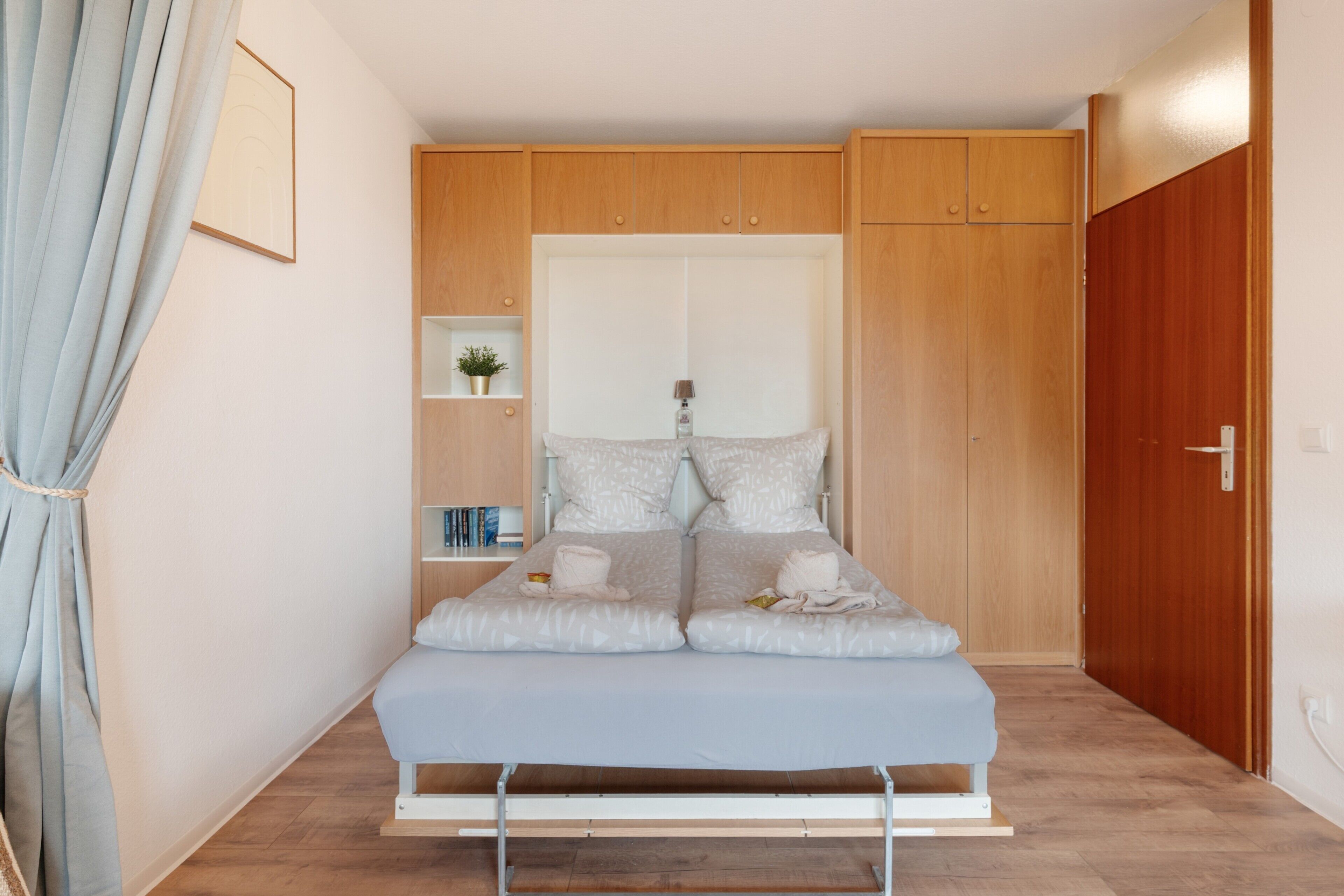 Un dormitorio pequeño y moderno con cama, armario, estantería con libros y una planta en maceta.