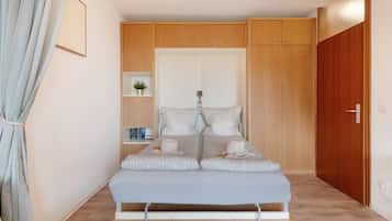 Un dormitorio pequeño y moderno con cama, armario, estantería con libros y una planta en maceta.