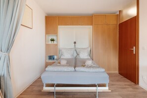 Een compacte, moderne slaapkamer met een bed, een kledingkast, een plank met boeken en een potplant.