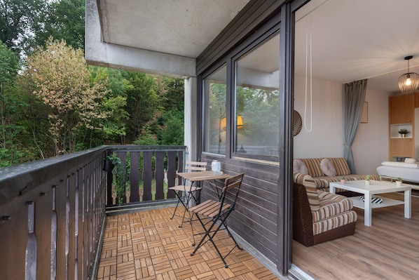 A balcony with a wooden table and chairs, a sofa, and a potted plant.