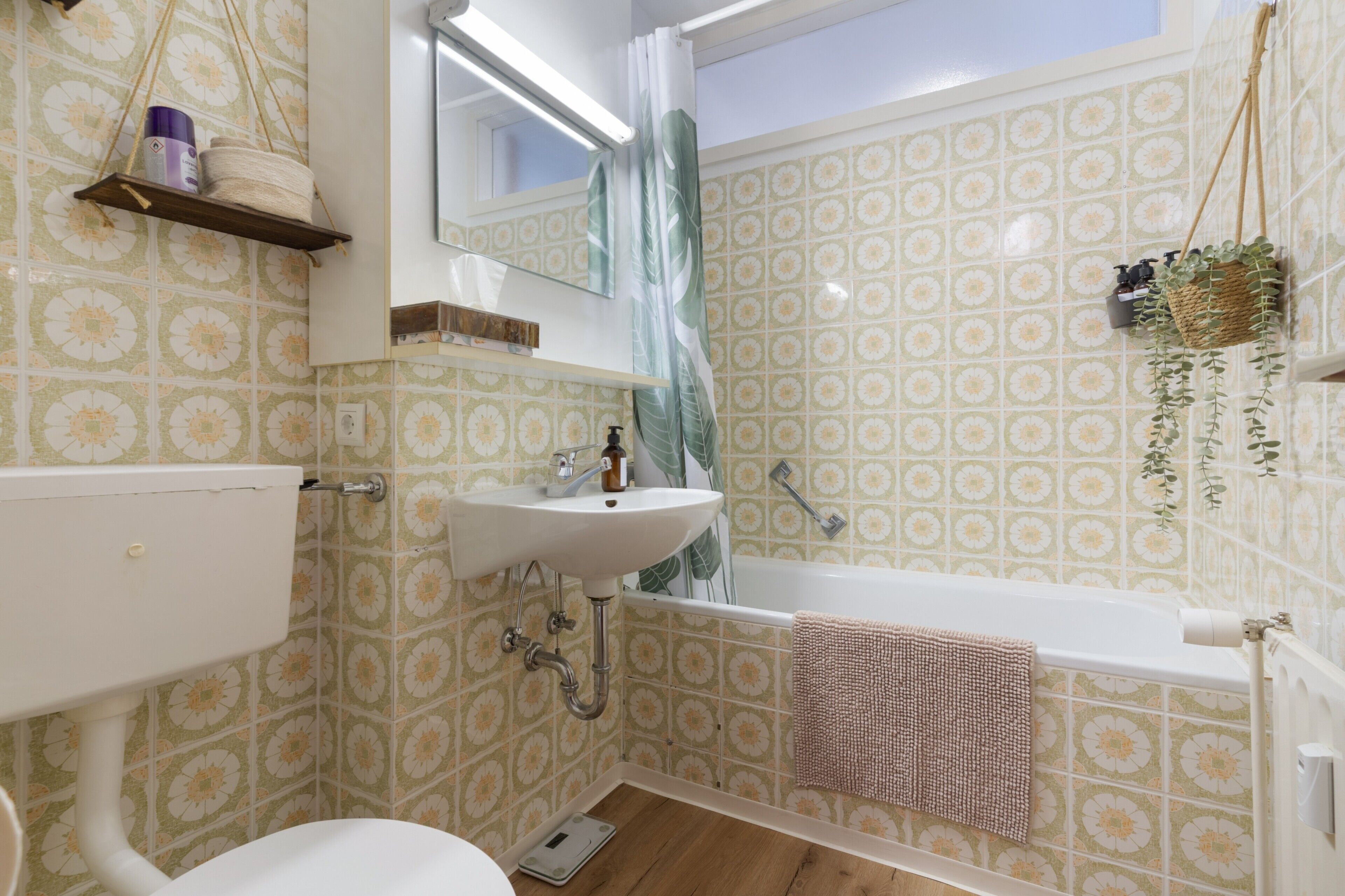 Ein Badezimmer mit Toilette, Waschbecken und Badewanne. Über dem Waschbecken hängt ein Spiegel, und ein Duschvorhang ist zu sehen.