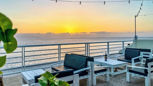 Ein Balkon mit weißer Möbel, Blick aufs Meer und Sonnenuntergang.