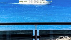 Ein Kreuzfahrtschiff auf dem Ozean, im Hintergrund eine gebirgige Insel.