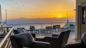 Ein Balkon mit Sitzgelegenheit im Freien, einer Bar und Blick auf das Meer bei Sonnenuntergang.
