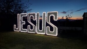 Illuminated letters spelling "JESUS" in a garden at dusk. - Serene Retreat at Garza’s Ranch - Ponies & Cows (Wallis)