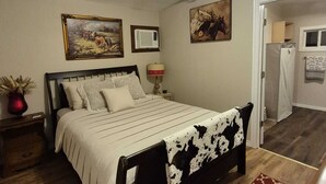 A bedroom with a bed, a nightstand, a lamp, and a painting on the wall. - Serene Retreat at Garza’s Ranch - Ponies & Cows (Wallis)