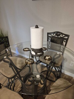 A round glass table with four chairs, each with a metal frame and cushioned seats. A large white paper towel roll is placed on the table. - Serene Retreat at Garza’s Ranch - Ponies & Cows (Wallis)