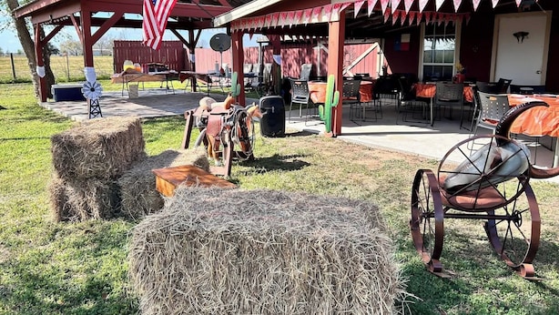 A rustic outdoor dining area with hay bales, a windmill, and a covered seating area with tables and chairs. - Serene Retreat at Garza’s Ranch - Ponies & Cows (Wallis)