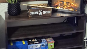 A television with a fireplace, a sign reading 'S'MORES Station,' and a shelf with board games. - Serene Retreat at Garza’s Ranch - Ponies & Cows (Wallis)