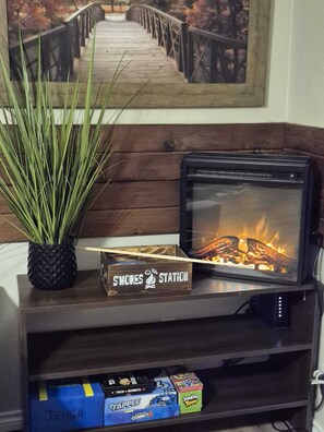A television with a fireplace, a sign reading 'S'MORES Station,' and a shelf with board games. - Serene Retreat at Garza’s Ranch - Ponies & Cows (Wallis)