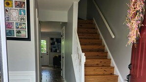 Un pasillo con una escalera de madera, piso de baldosas y una puerta con marco rojo.