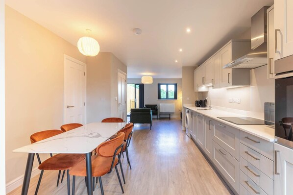 A modern kitchen with white cabinets, a stainless steel range hood, and a dining area with a white table and orange chairs. - Newly Refurbished Home, Short Drive to Bath Centre (Bath and North East Somerset)