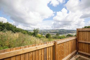 A wooden fence overlooking a landscape with a distant town and cloudy sky.