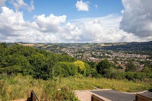 A panoramic view of a town with rolling hills, dense greenery, and a clear sky.