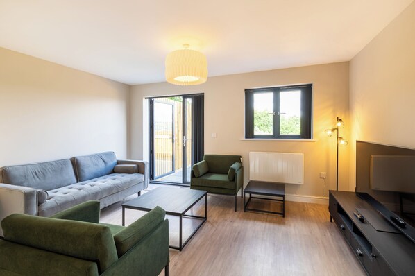 A modern living room with a sofa, armchairs, a coffee table, a TV, and a radiator.