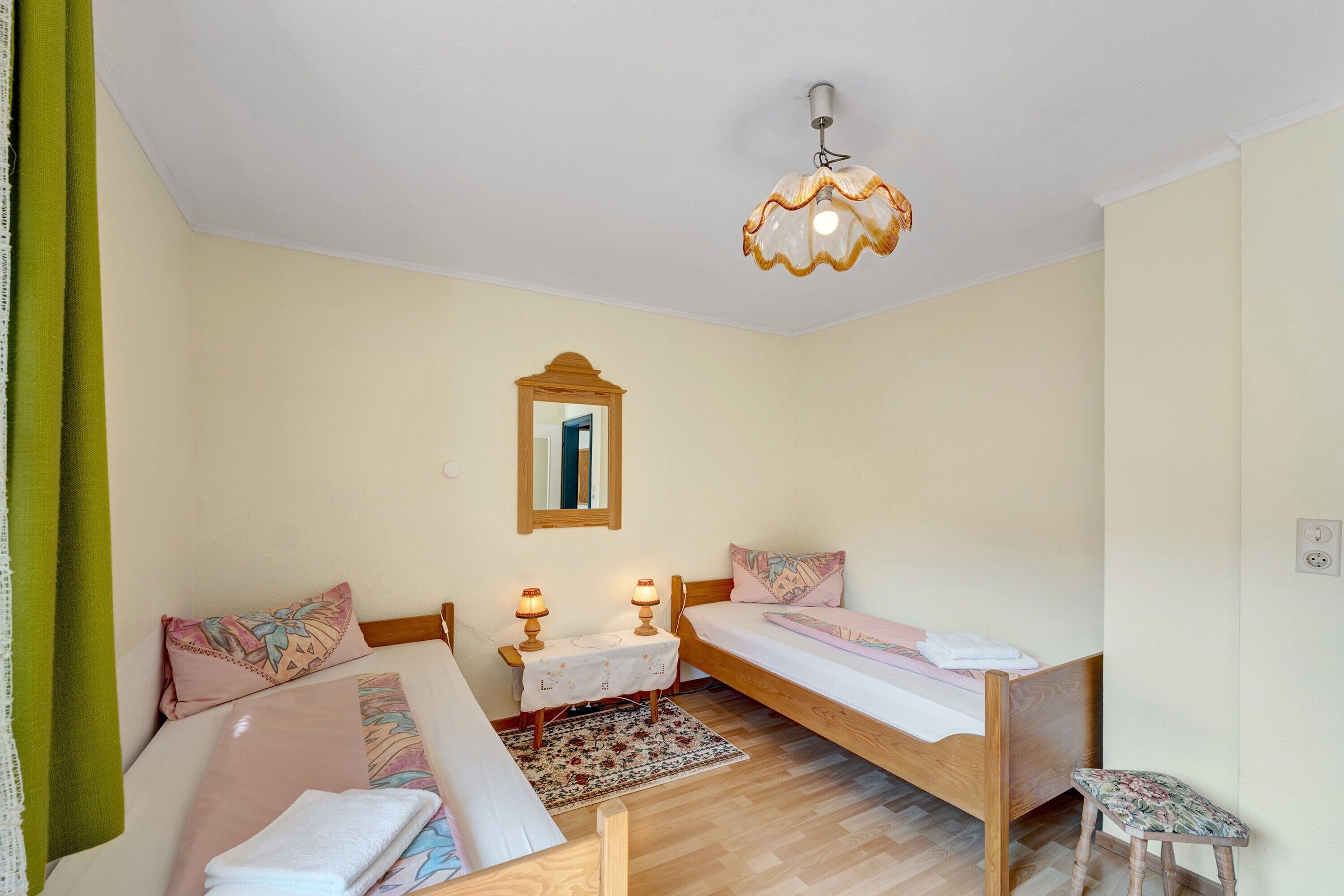 A bedroom with two single beds, a bedside table with lamps, a mirror, and a small stool.