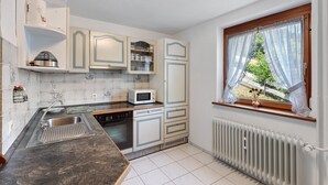 A compact kitchen with white cabinets, a microwave, and a window with a view of greenery. - Apartment 'Harter' with Shared Terrace, Shared Garden and Wi-Fi (Wolfach)