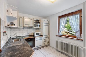 A compact kitchen with white cabinets, a microwave, and a window with a view of greenery. - Apartment 'Harter' with Shared Terrace, Shared Garden and Wi-Fi (Wolfach)