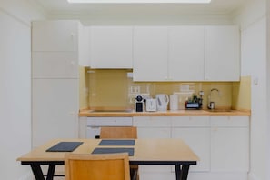 Una cocina compacta con armarios blancos, encimera de madera, un lavamanos y una mesa de comedor con sillas.