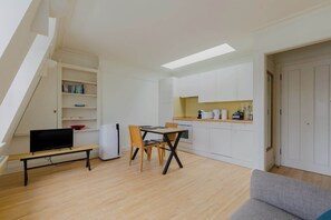 Un apartamento pequeño con comedor, kitchenette y un televisor sobre una mesa de madera.