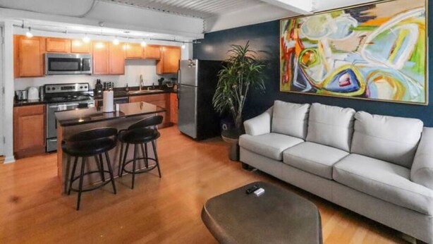 A modern kitchen with wooden cabinets, a central island with stools, and a large abstract painting on the wall.