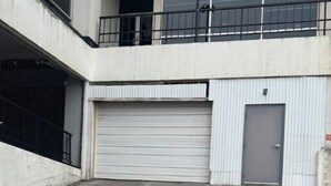 A building with a closed garage door, a balcony with a metal railing, and a concrete ground.